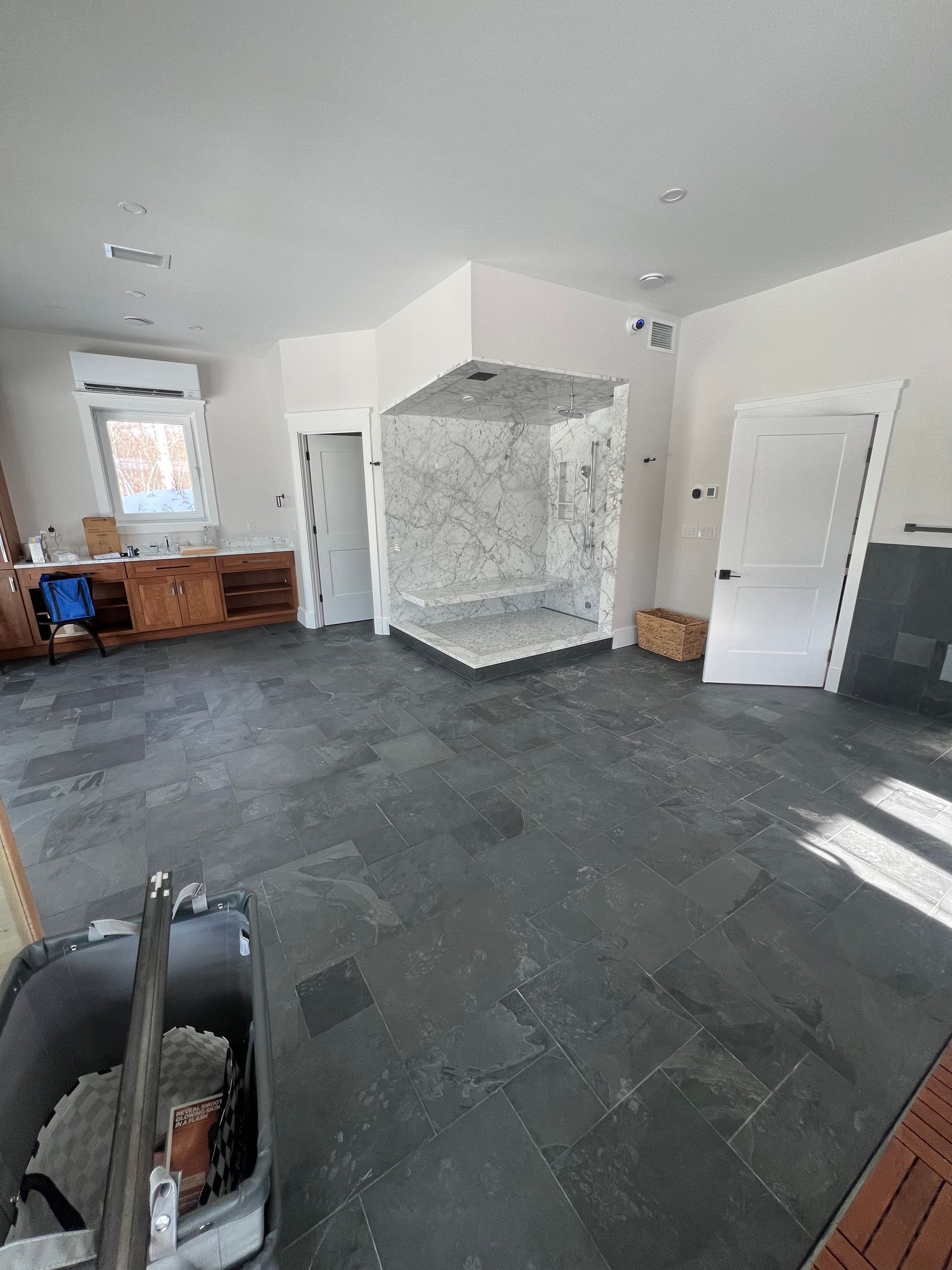 A room under renovation featuring dark slate tile floors, white walls, a marble shower stall, and a wooden counter area.