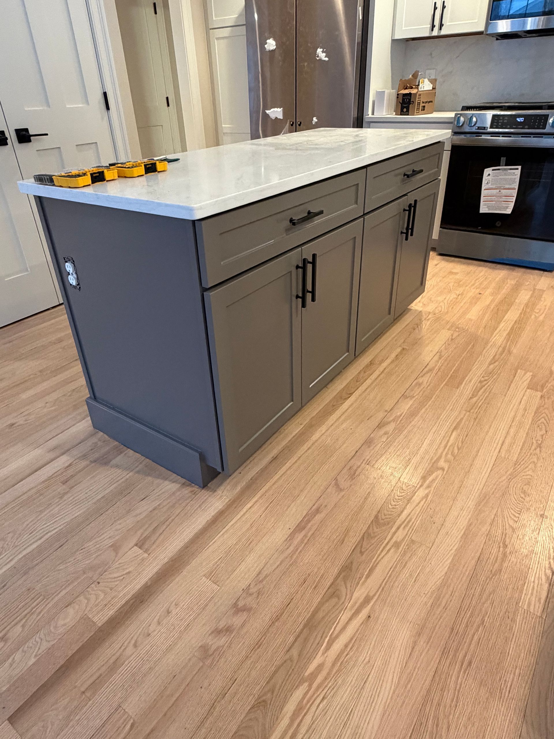 A dark gray kitchen island with a white countertop and black hardware, situated on light hardwood floors.