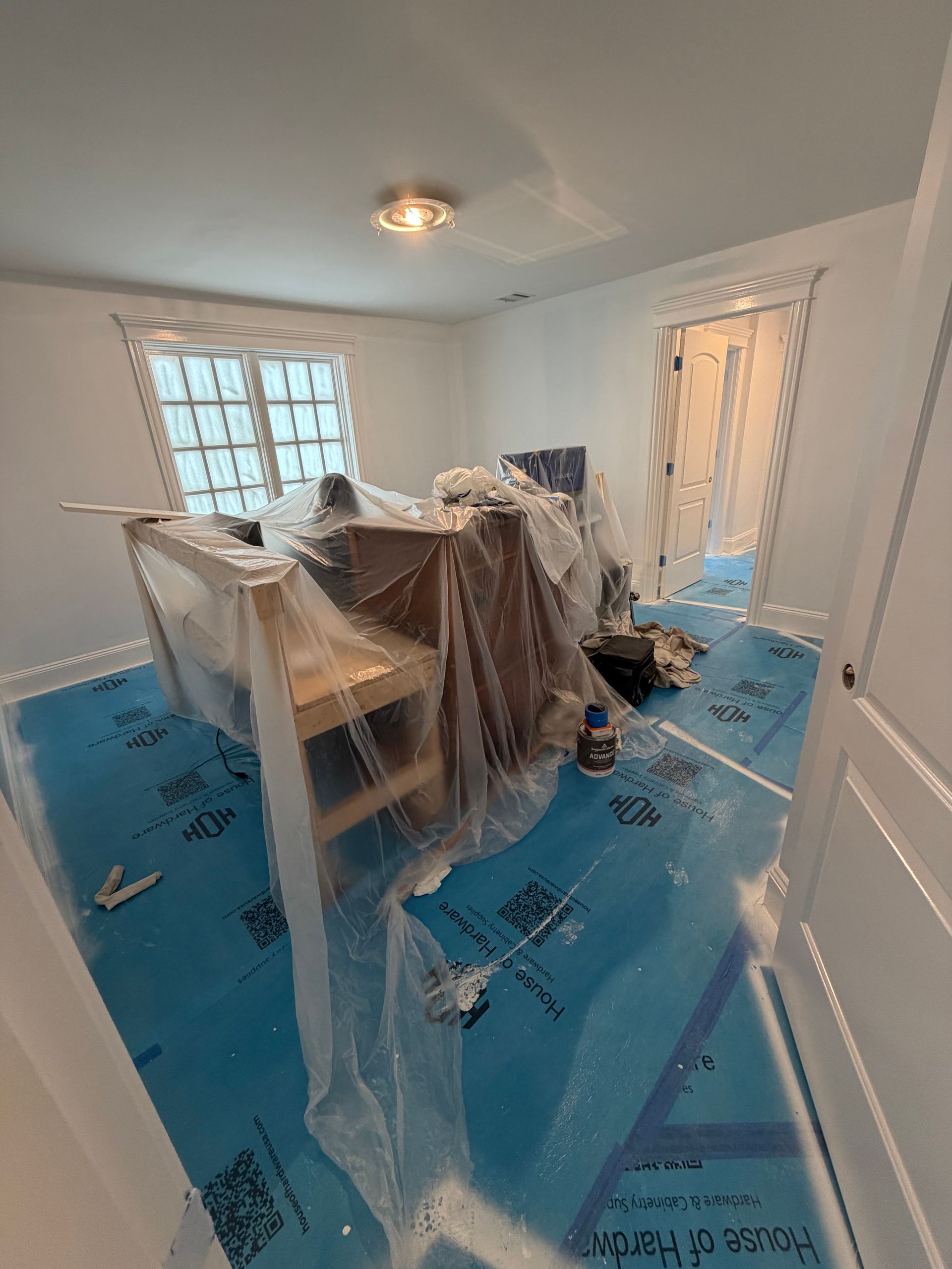 A room under renovation with blue protective floor covering and furniture draped in plastic.