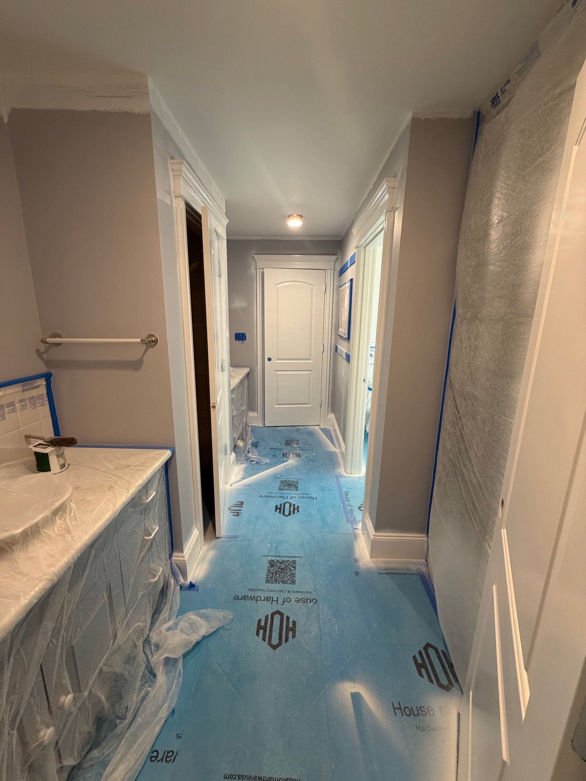 A bathroom hallway undergoing renovation with gray walls, protective plastic on surfaces, and blue floor covering.