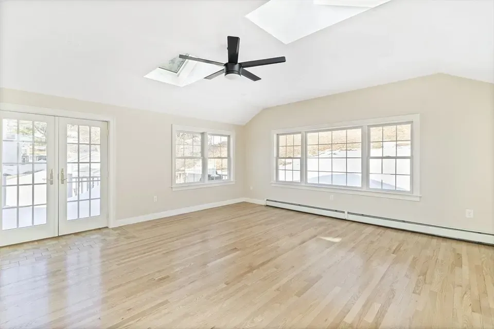 Bright, empty room with light hardwood floors, white walls, large windows, a ceiling fan, and a glass door to the outside.
