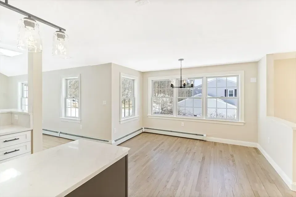 A bright, open dining area with light hardwood floors, neutral walls, large windows, and a modern chandelier.