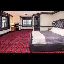 A bedroom with a large black tufted bed, red plaid carpet, dark wood trim, and windows overlooking a snowy scene.