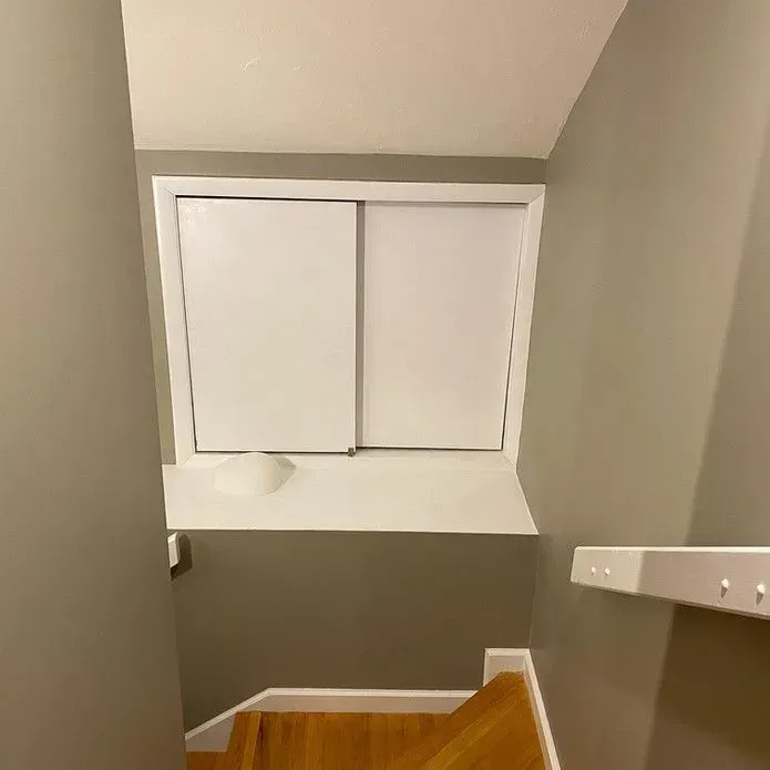 A light-colored window set into a gray wall at the top of a wooden staircase.