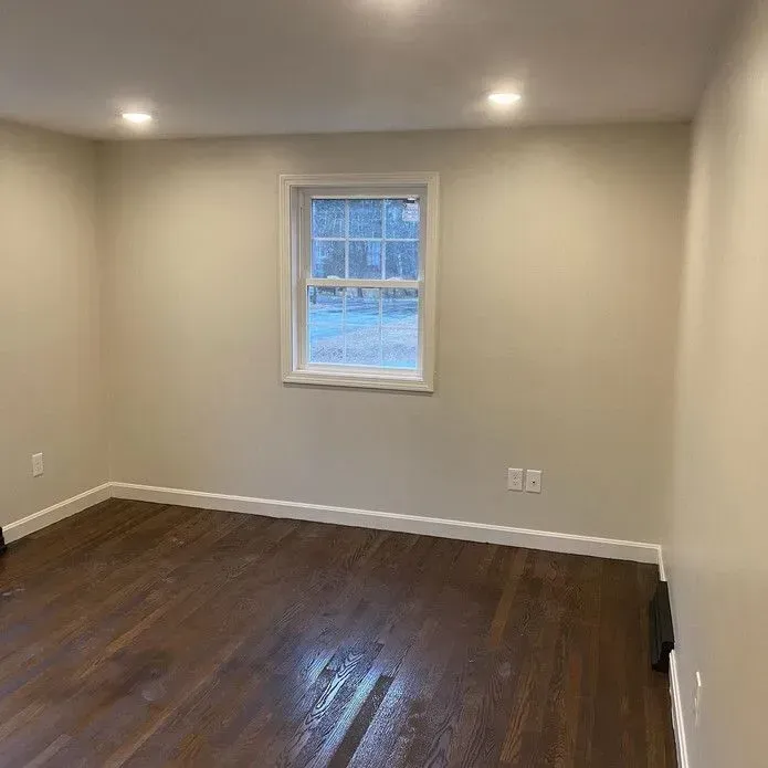 Empty room with light walls, a centered window, dark hardwood floors, and recessed lighting.
