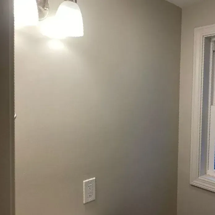 A light grey wall features a mounted wall light with two glass shades and a single electrical outlet below it.