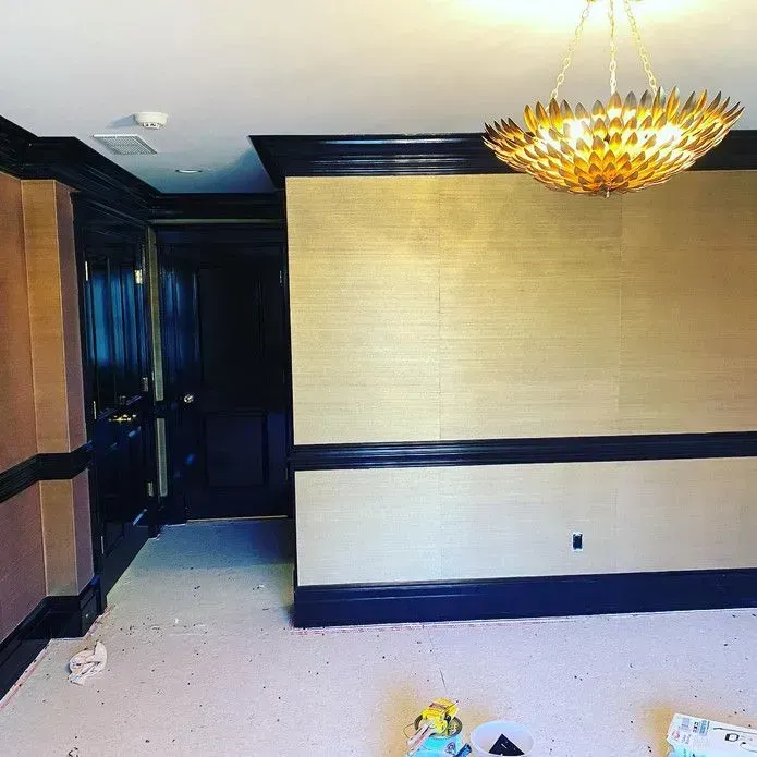 A gold-toned, textured wallpapered room features glossy black crown molding, chair rail, and baseboards under a gold light.