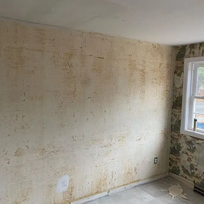 A room interior shows a wall with remnants of old wallpaper, partially stripped to expose the beige backing.