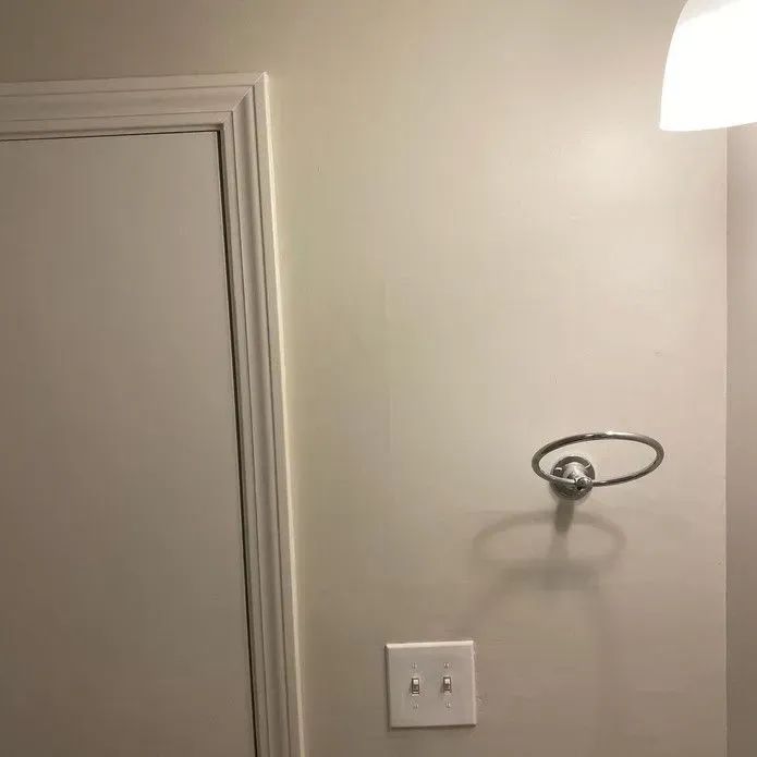 A wall-mounted chrome towel ring next to a light switch and a white door frame, illuminated by a nearby light fixture.