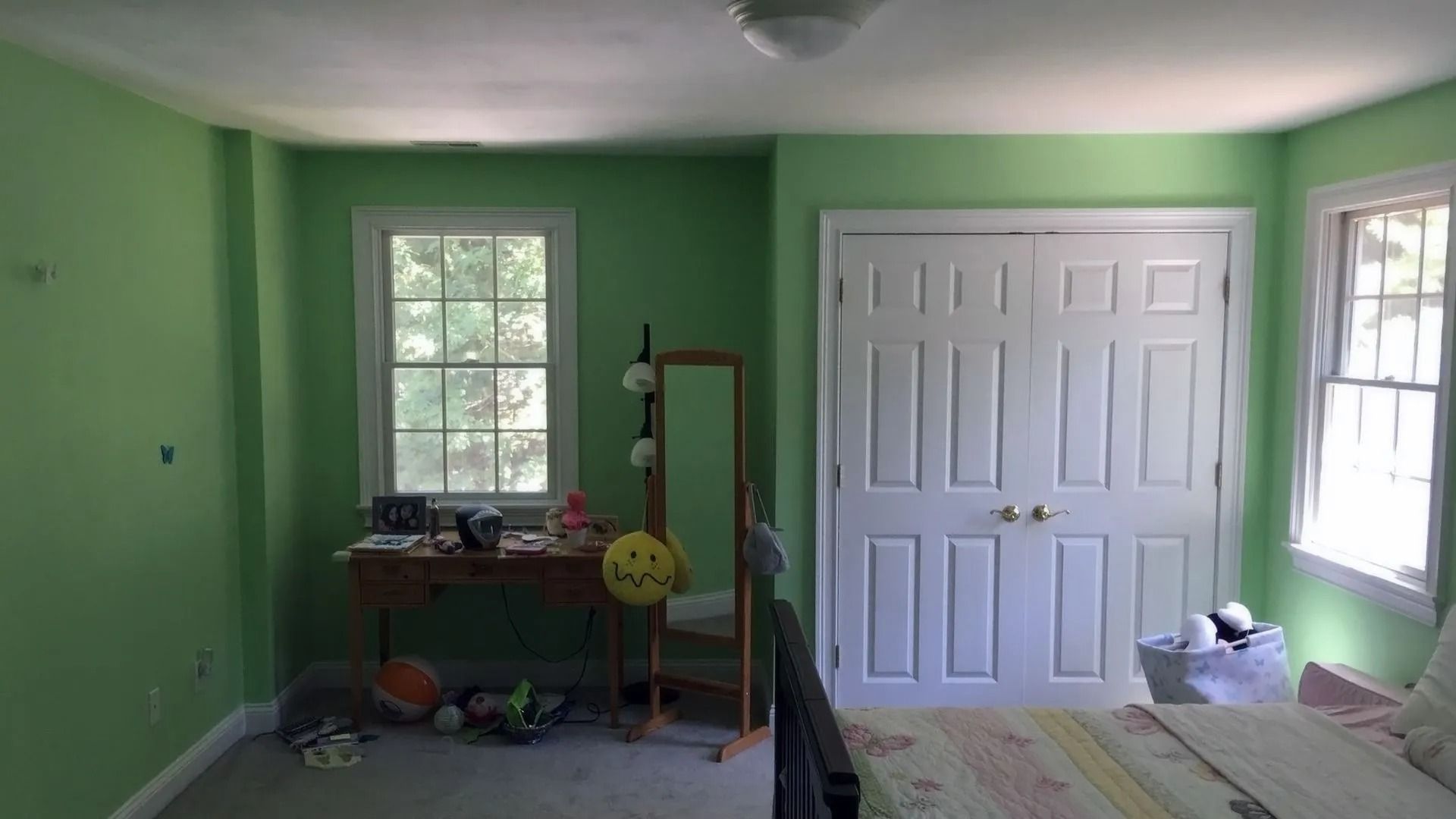 A bedroom with green walls, two windows, a white double closet, a desk, a full-length mirror, and a bed.