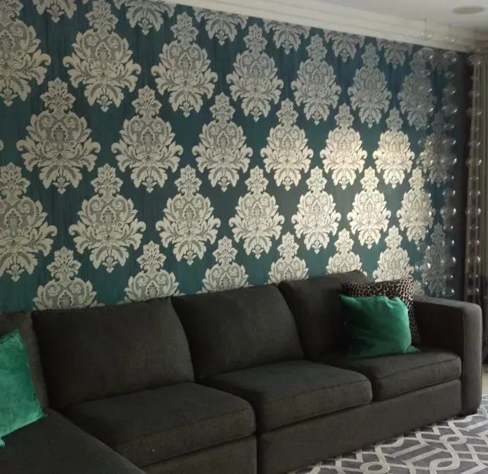 A charcoal sofa sits in front of a teal wall with a large-scale white damask pattern and a patterned area rug.