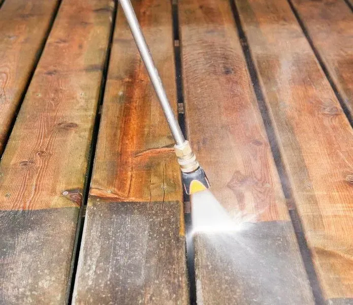 A pressure washer nozzle spraying a stream of water to clean dirt off wooden deck planks.