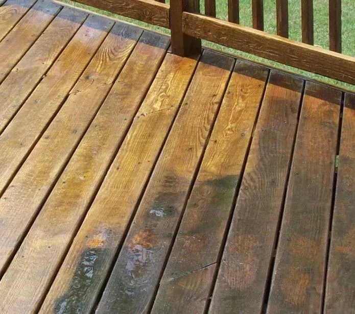 A wooden deck shows a clear contrast between cleaned, light-colored boards and uncleaned, dark, weathered boards.