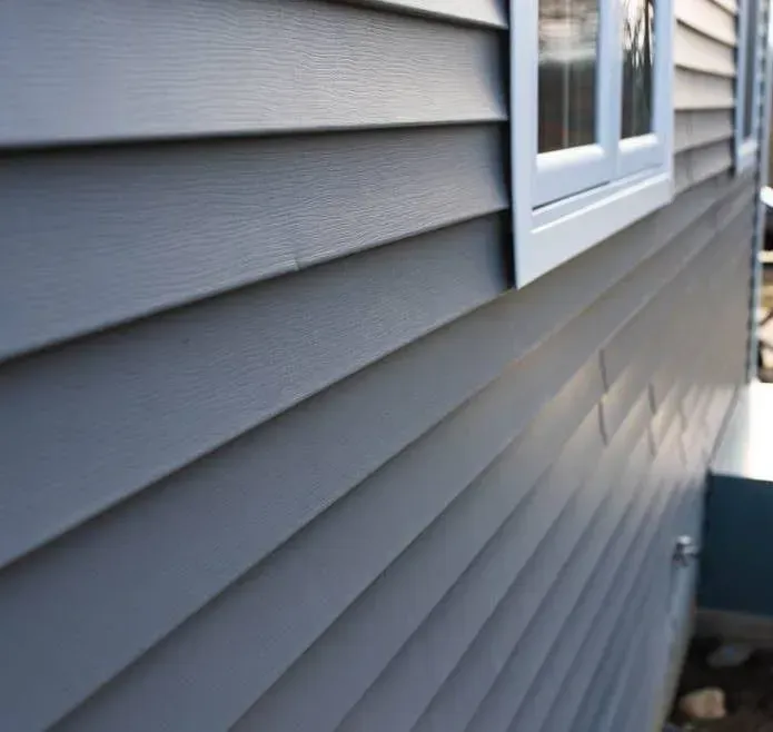 Close-up of horizontal grey vinyl siding on the exterior wall of a house next to a window frame.