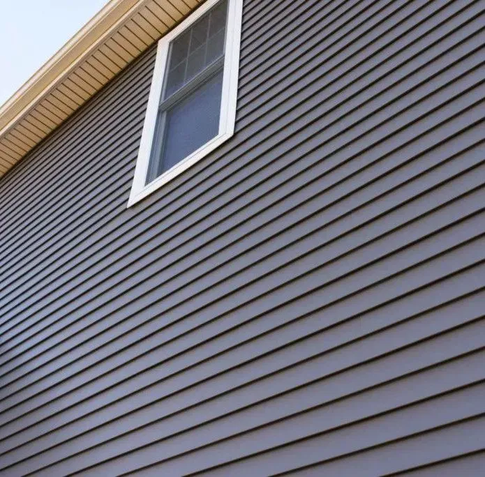 A single window set into a dark gray house wall with horizontal siding and a beige soffit overhang.