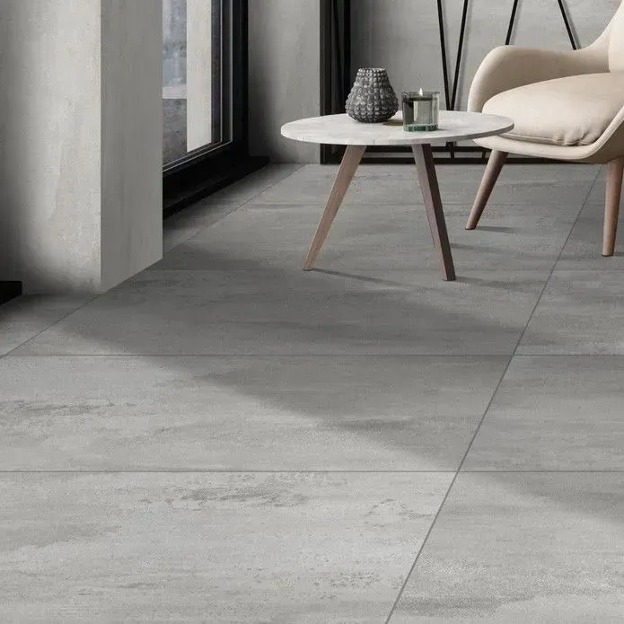 A minimalist interior featuring large grey concrete-look floor tiles, a small round table, and a pale armchair.