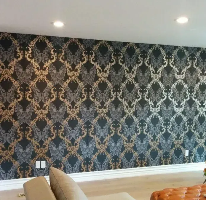 An accent wall covered in dark wallpaper featuring a repeating, ornate gold and silver damask pattern.