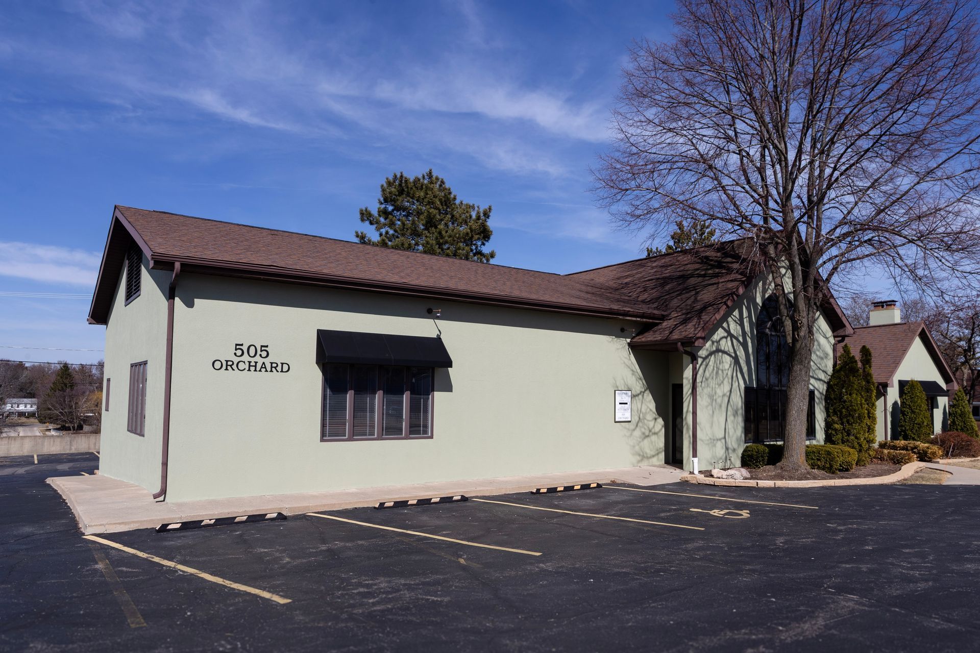 A green building with a brown roof and a parking lot in front of it