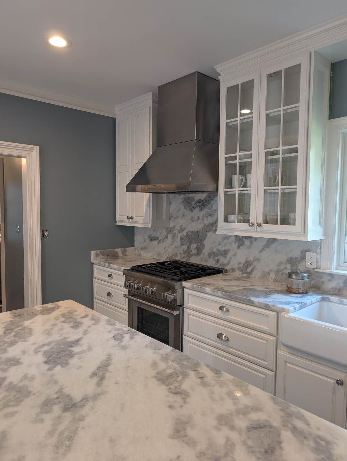 A kitchen with white cabinets, a stove, a sink, and a hood.