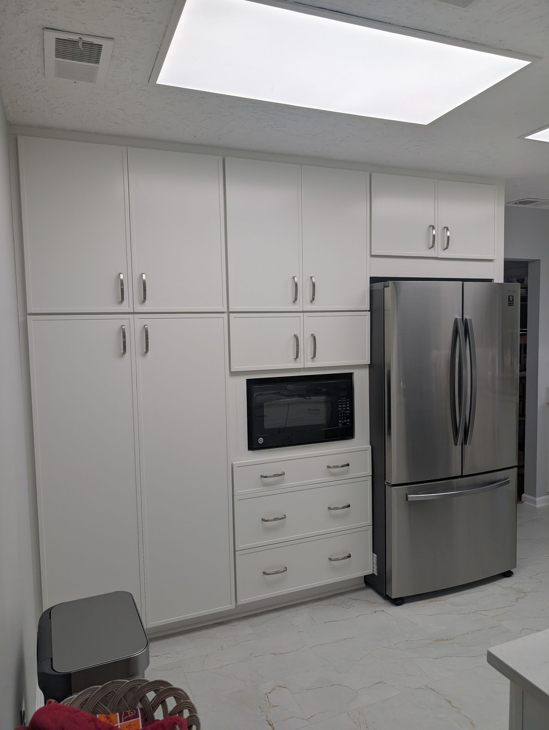 White kitchen cabinets with a built-in microwave and a stainless steel refrigerator.