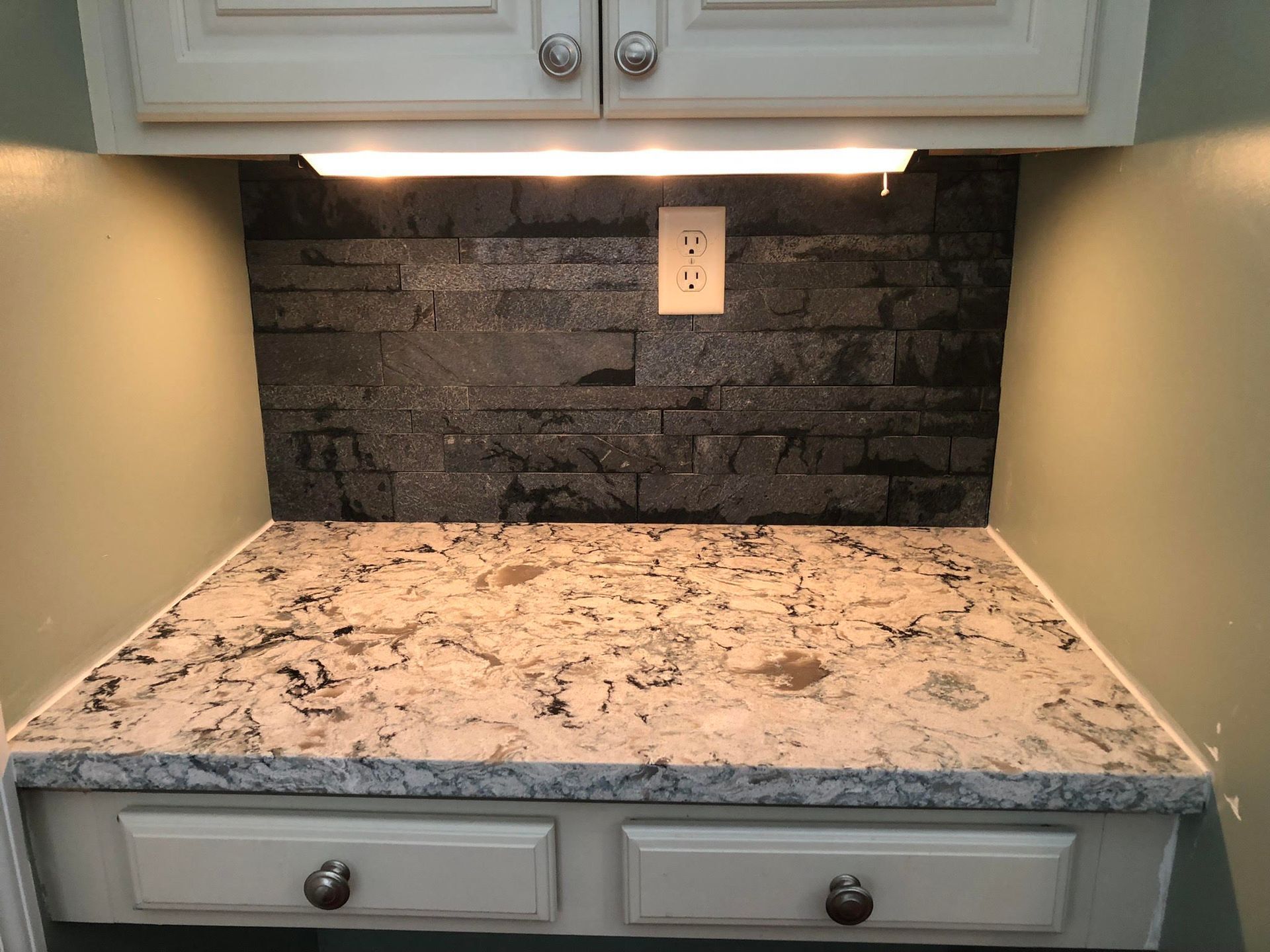 A kitchen counter with a granite counter top and a brick wall behind it.