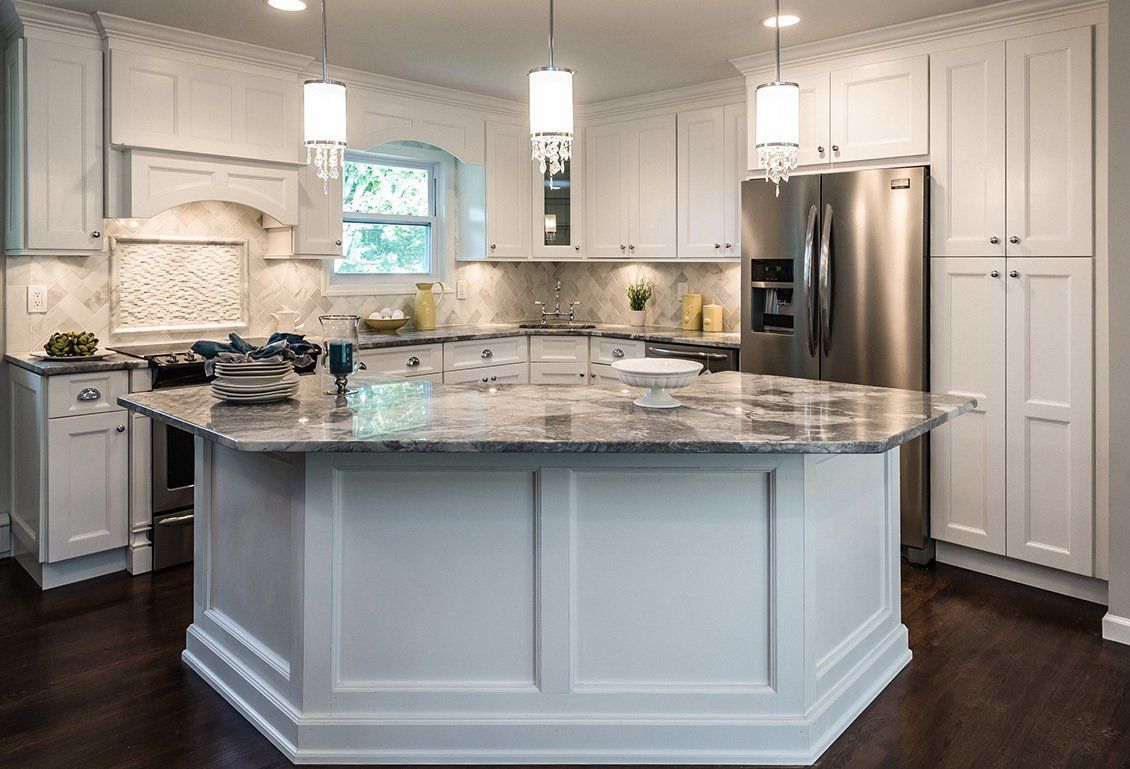 A kitchen with white cabinets , granite counter tops , stainless steel appliances and a large island.