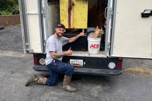 Man kneeling by the open back of a box truck, pointing at equipment inside a storage area.