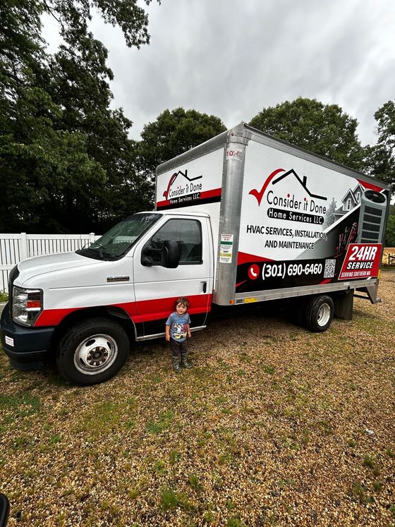 White-and-red box truck with tree service branding parked on grass beside trees