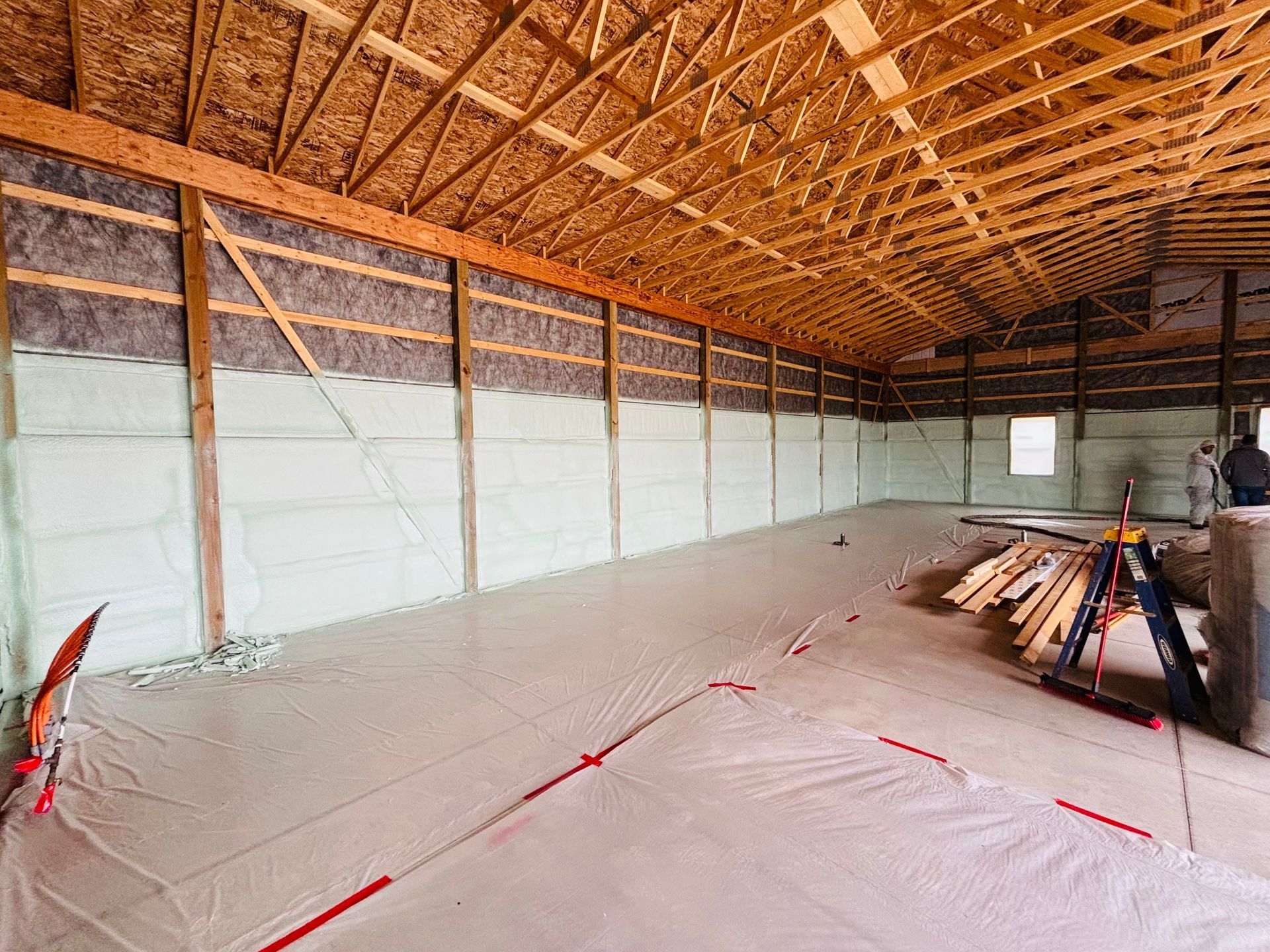 Interior of a large building under construction, walls and ceiling insulated with spray foam, covered floor.