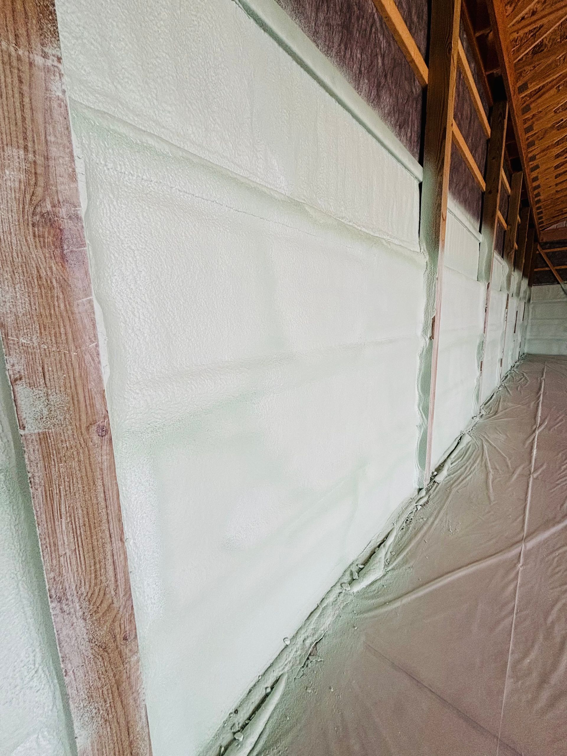 Wall being insulated with light green spray foam between wooden beams.