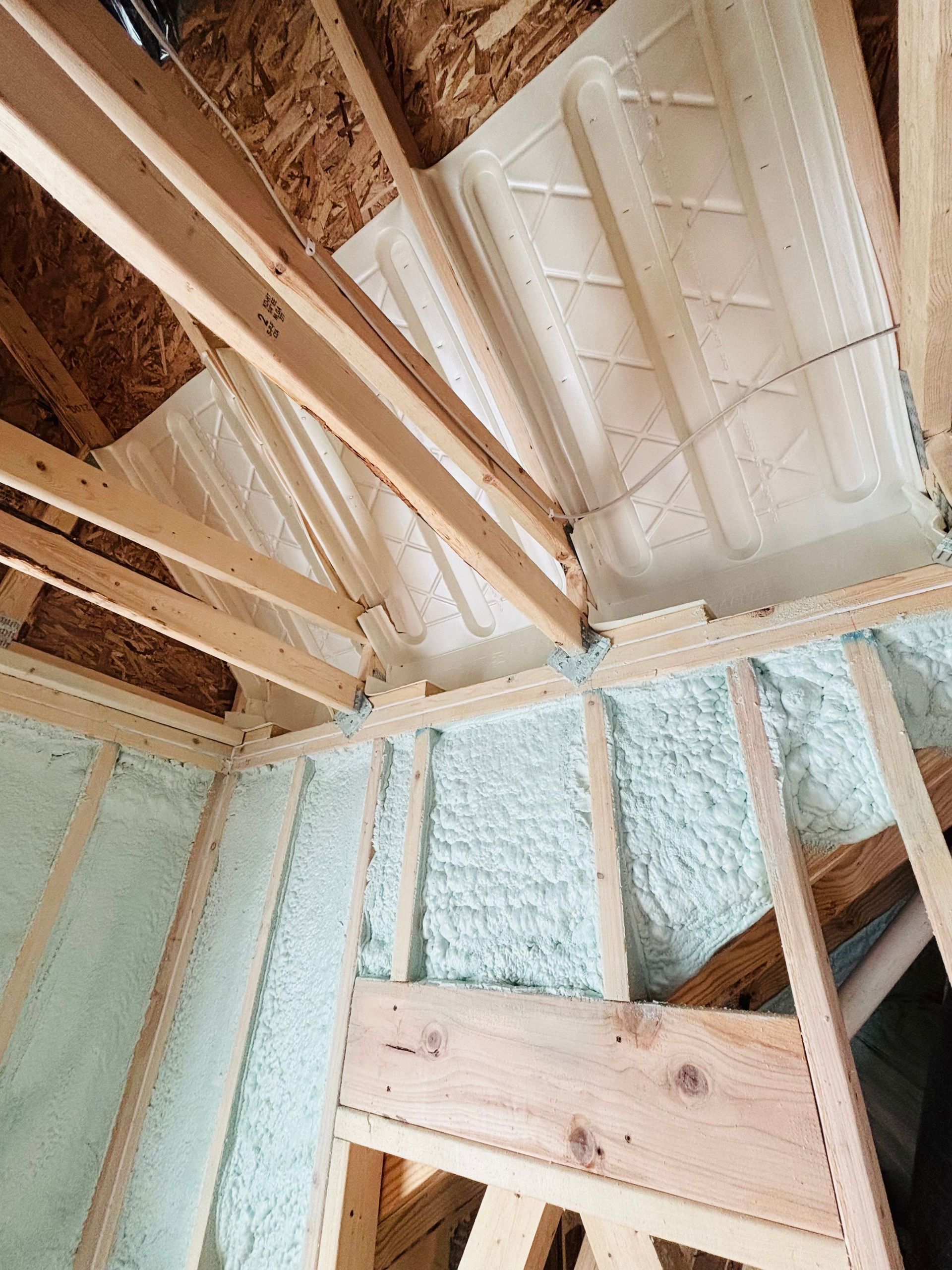 Spray foam insulation in a wooden attic frame, light blue-green and white colors.