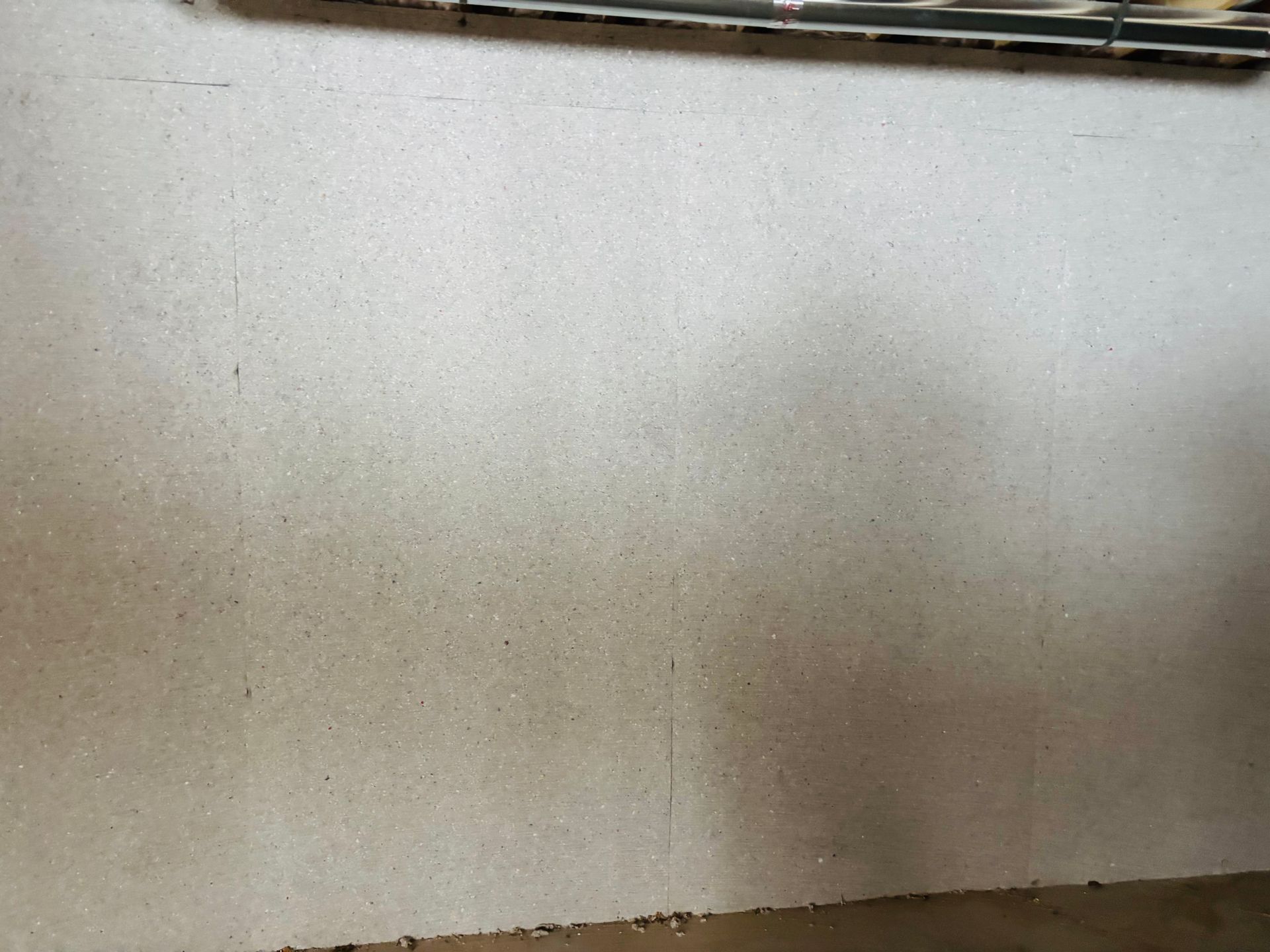 Close-up of a textured, light-colored wall with small dark specks and a darker lower edge.