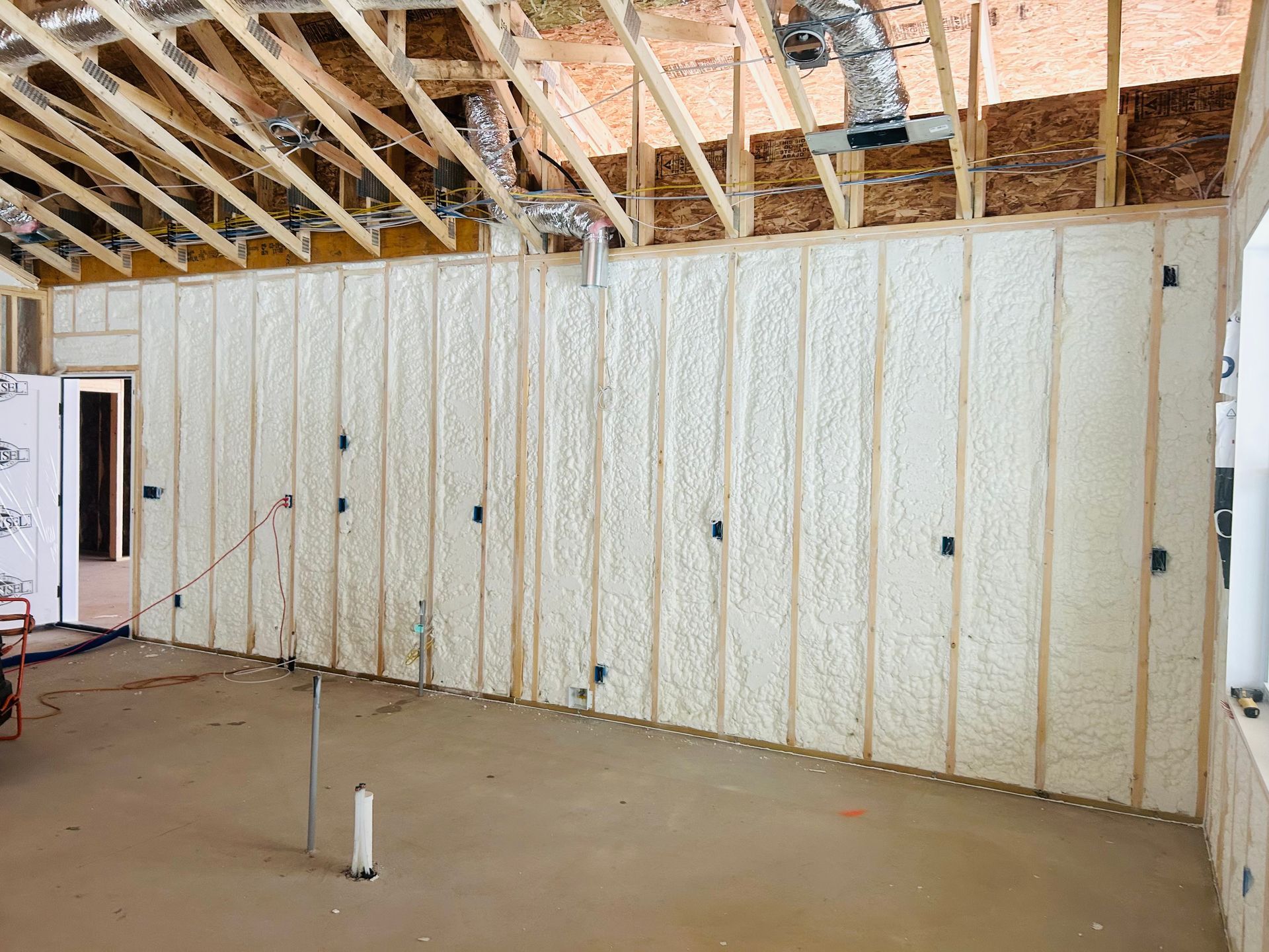 Interior of a room under construction with spray foam insulation on the walls. Wooden beams and unfinished ceiling visible.