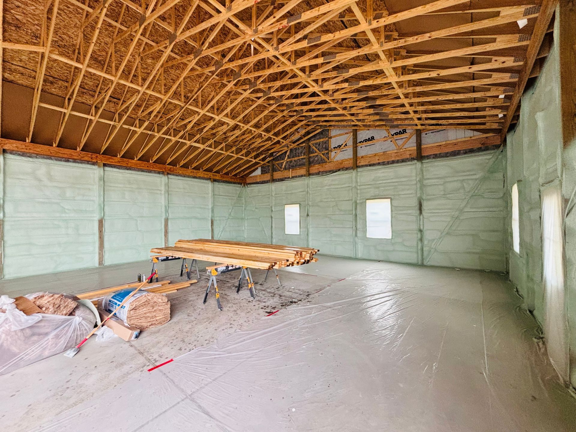 Interior of a building under construction, showing a concrete floor, spray foam insulation, and exposed wood rafters.