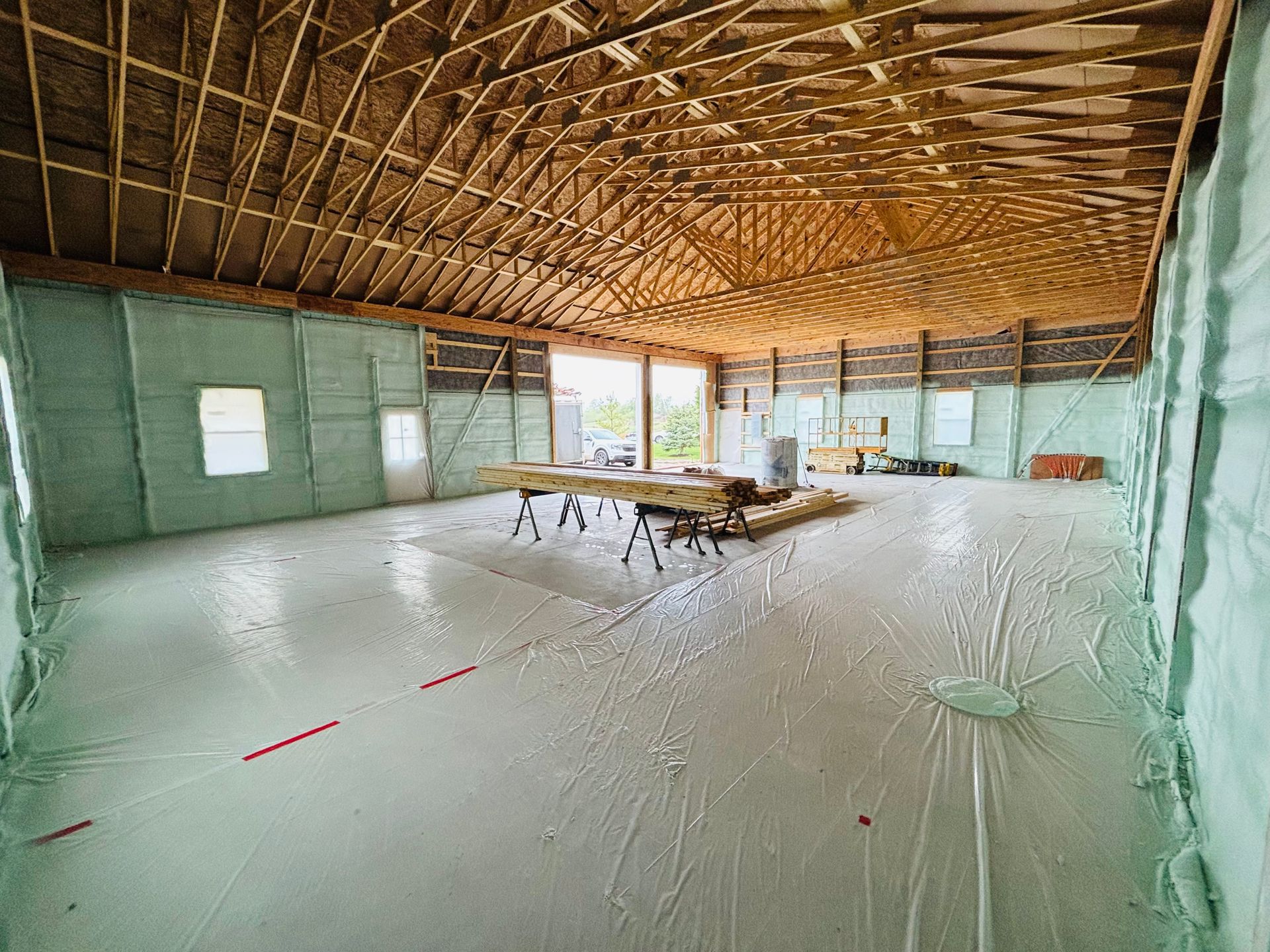 Interior of a building under construction, walls and ceiling insulated with foam, concrete floor covered with plastic.
