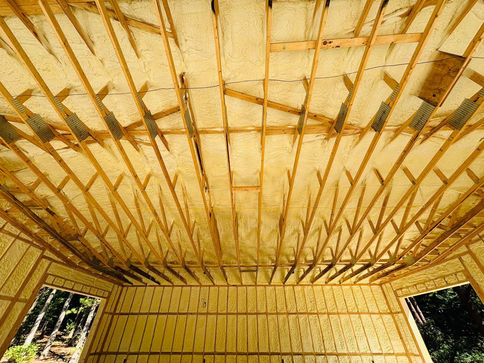 Interior of a building under construction, showing wooden rafters and spray foam insulation.