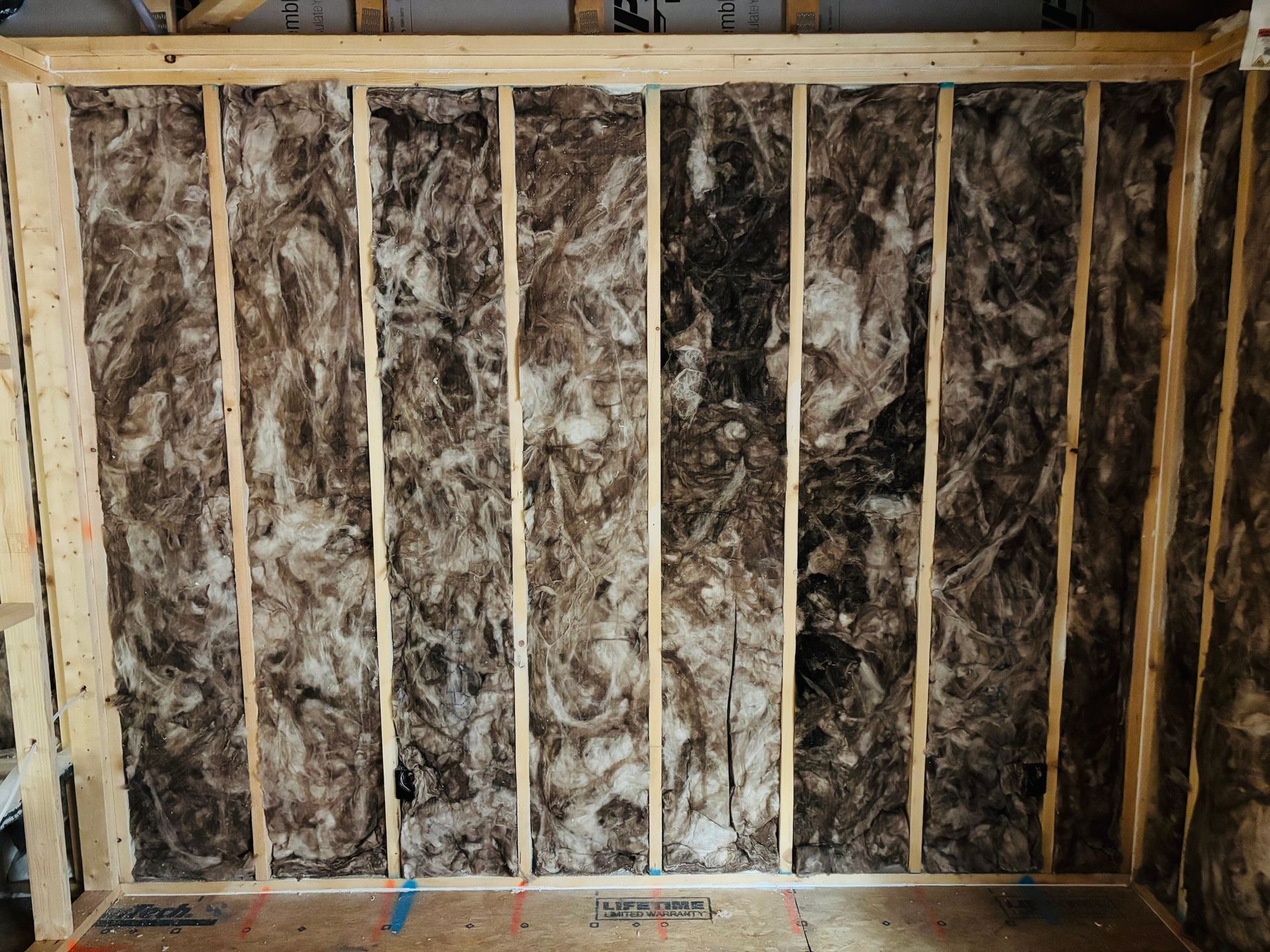 Insulated wall frame with wood studs and dark-colored insulation, ready for drywall.
