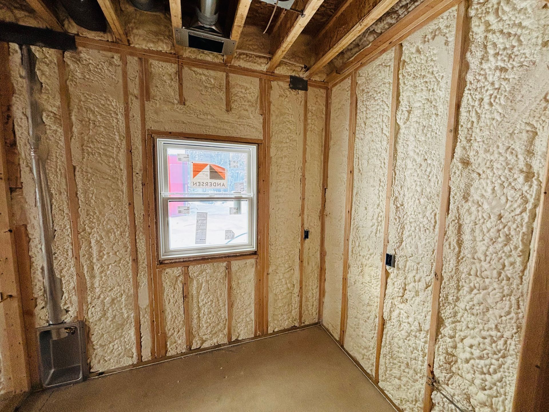 Interior room with spray foam insulation between wooden studs, window in the center.