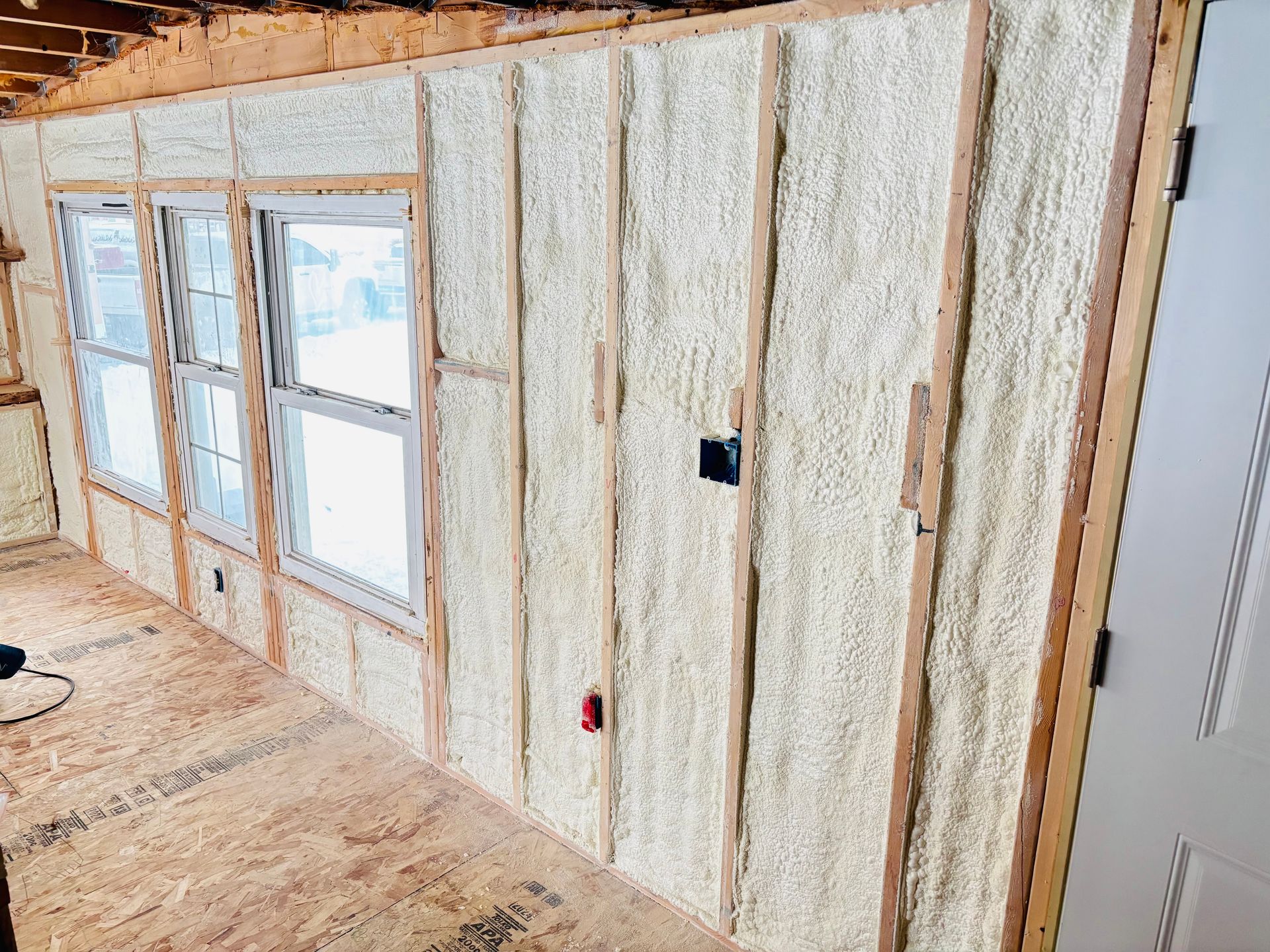 Interior wall with insulation, studs visible. Windows and door frames are also visible, room under construction.