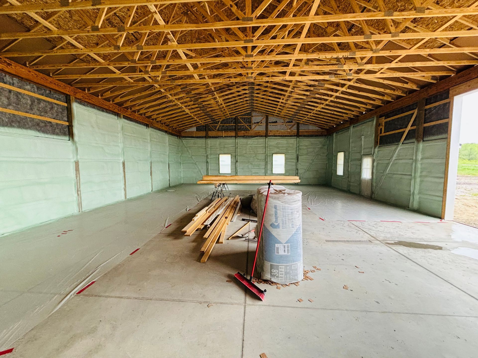 Interior of a new building under construction, featuring concrete floor, green insulation, and wooden rafters.