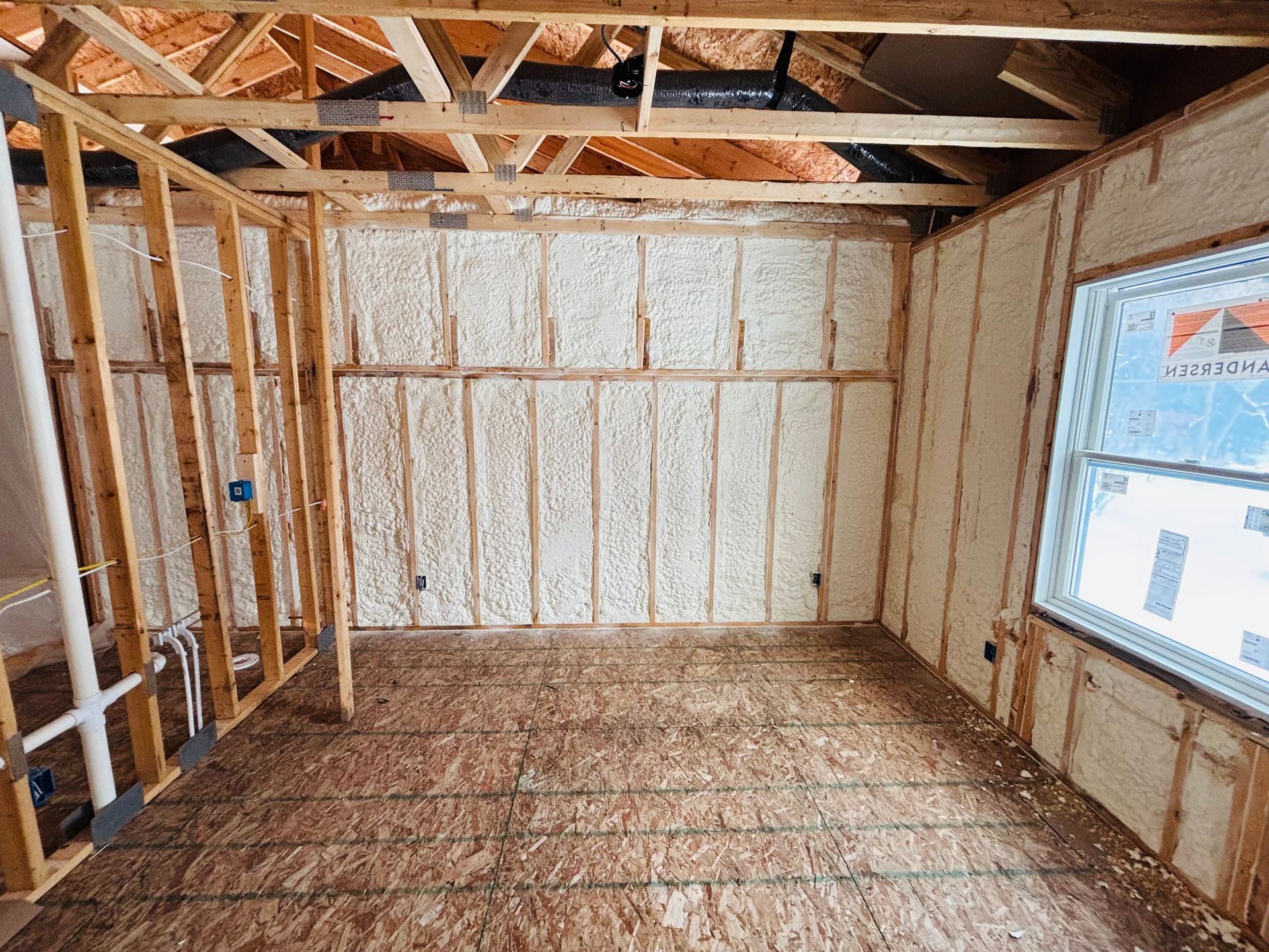 Interior of a room under construction with exposed wooden framing and walls insulated with spray foam.
