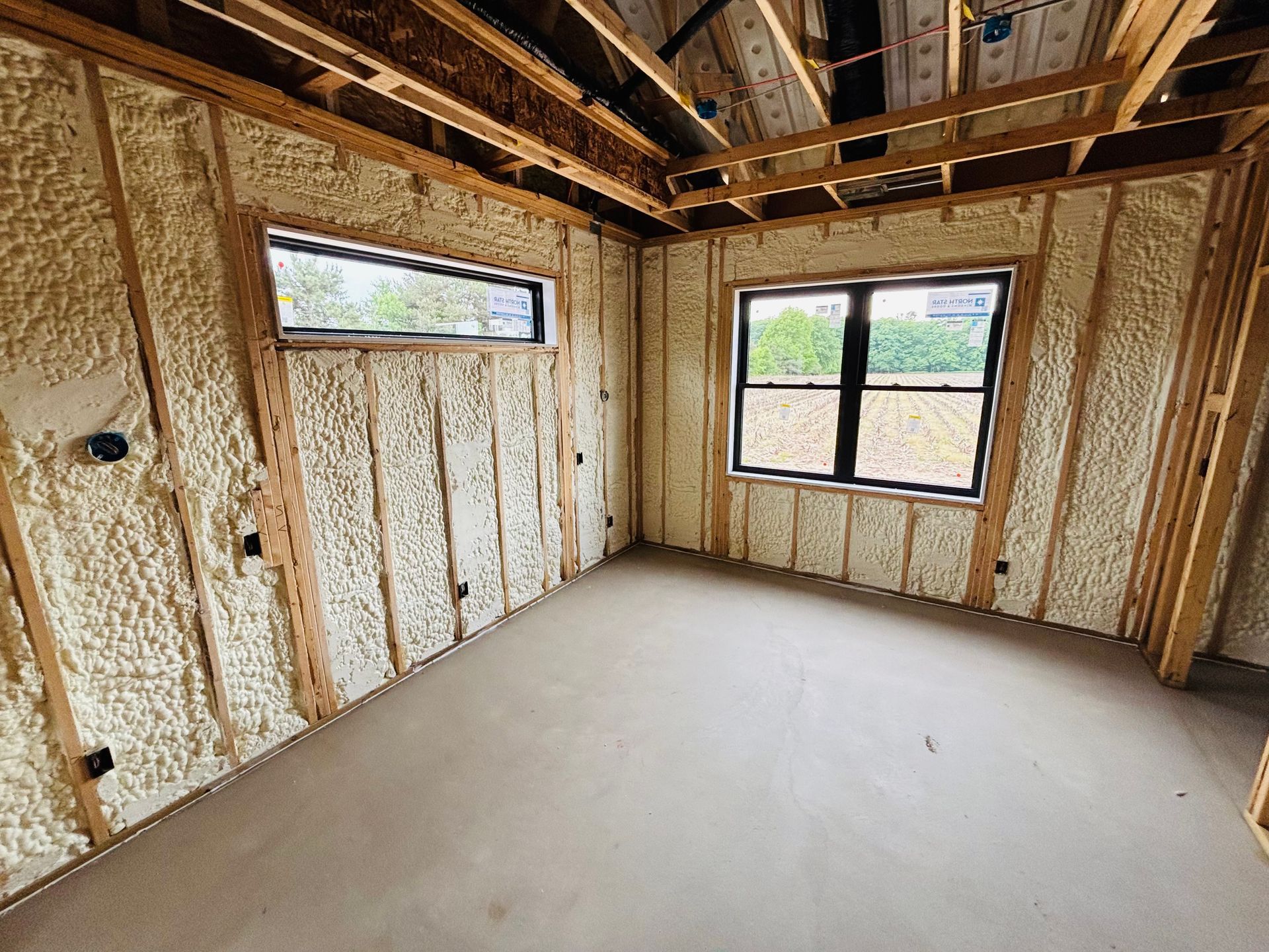 Interior of a room with exposed wooden framing and walls insulated with spray foam. Two windows are visible.