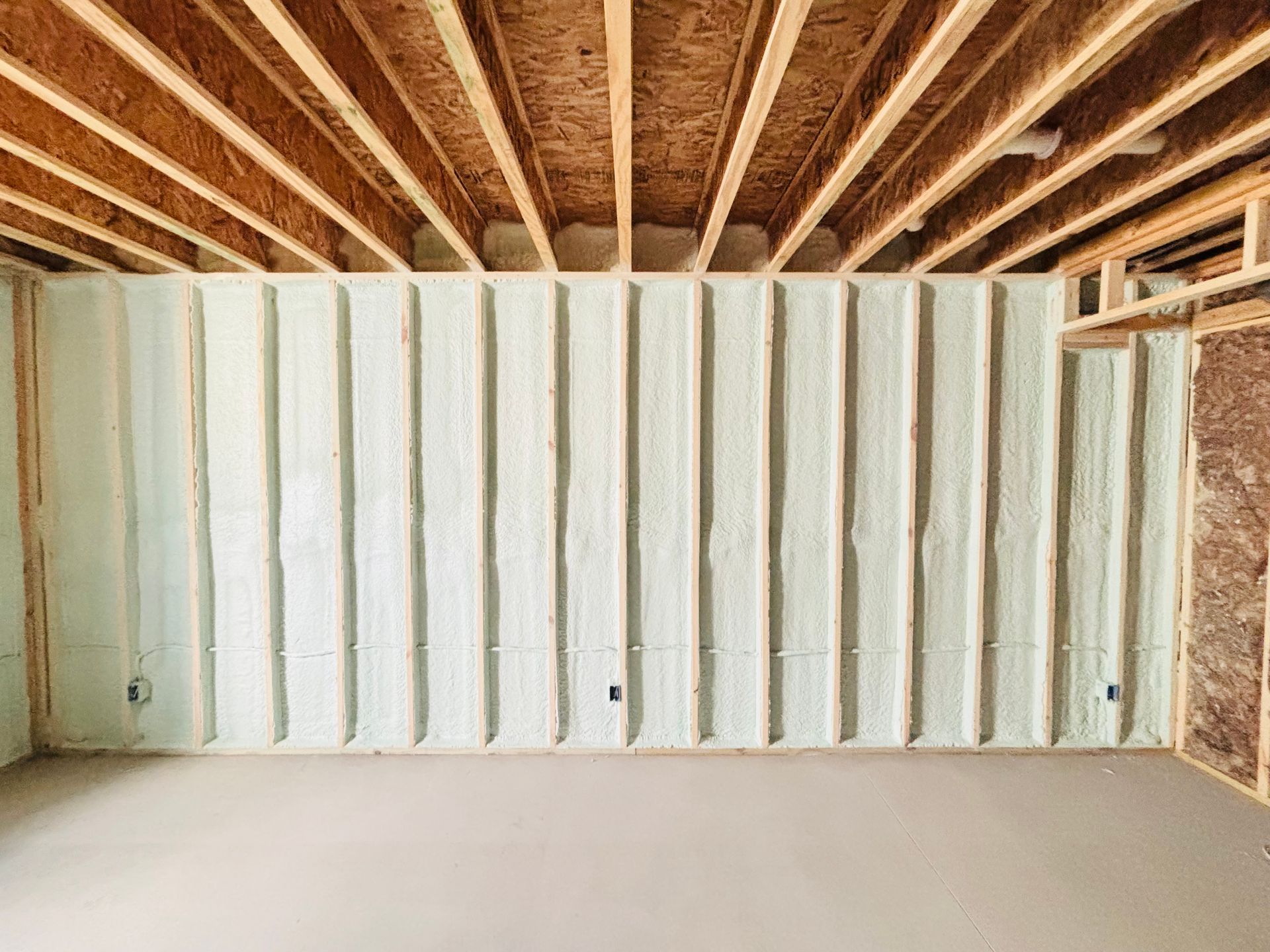 Interior view of a room under construction, with spray foam insulation between wooden studs, and unfinished ceiling.
