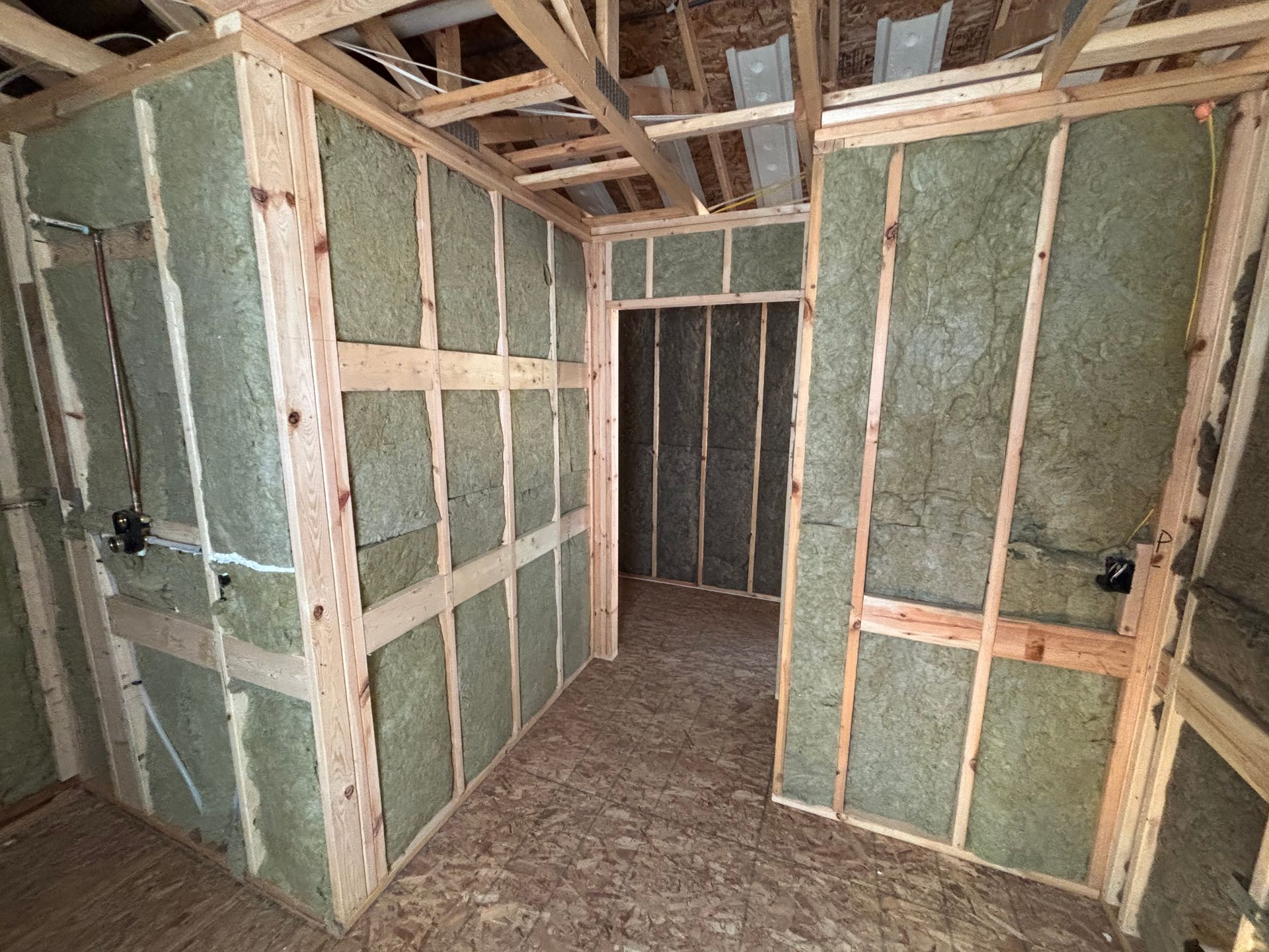 Interior construction: wooden framing, insulation, and unfinished walls in a room, with doorways and exposed beams.