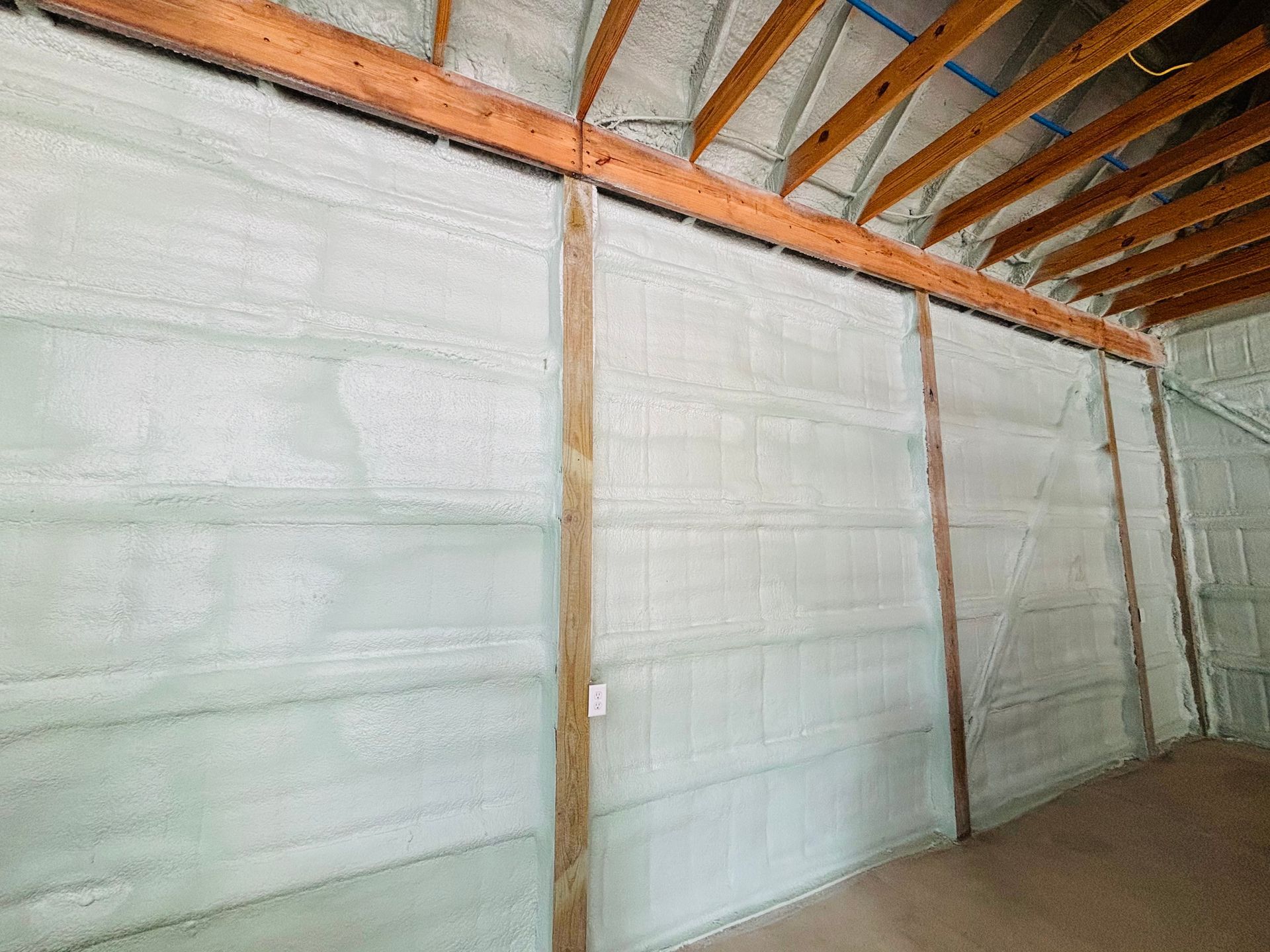 Interior wall covered in light green spray foam insulation, with exposed wooden beams.