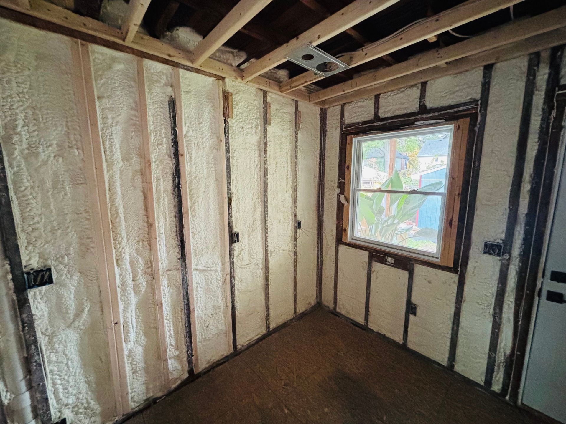 Room interior with spray foam insulation on walls, window, wooden beams.