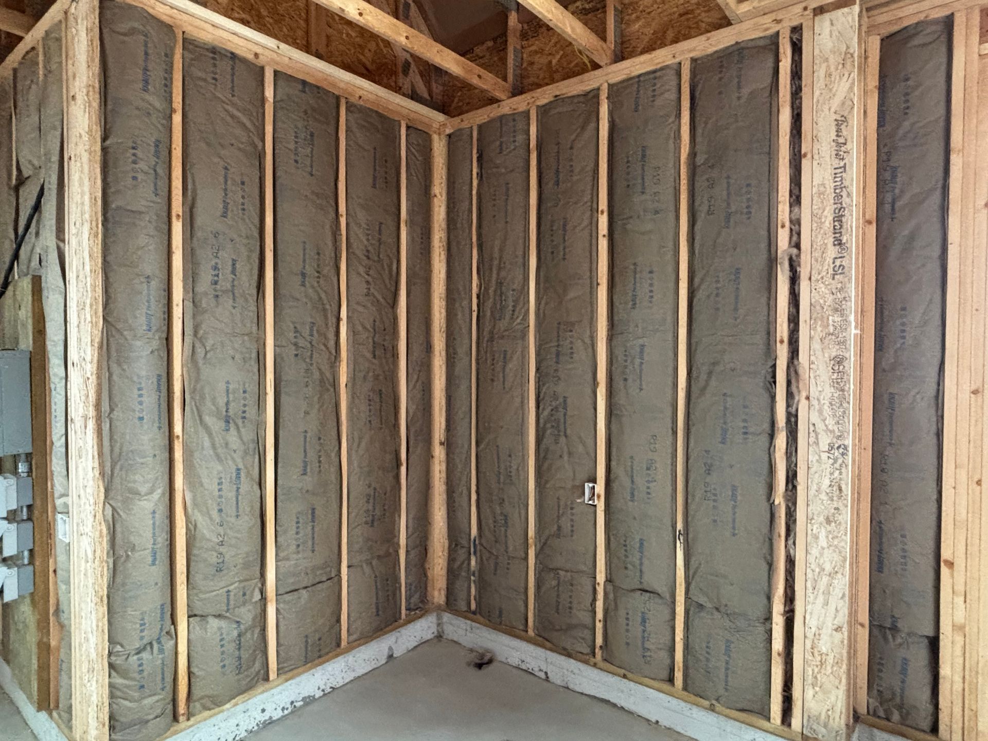 Interior corner of a room under construction, with wooden frame, insulation, and concrete base.