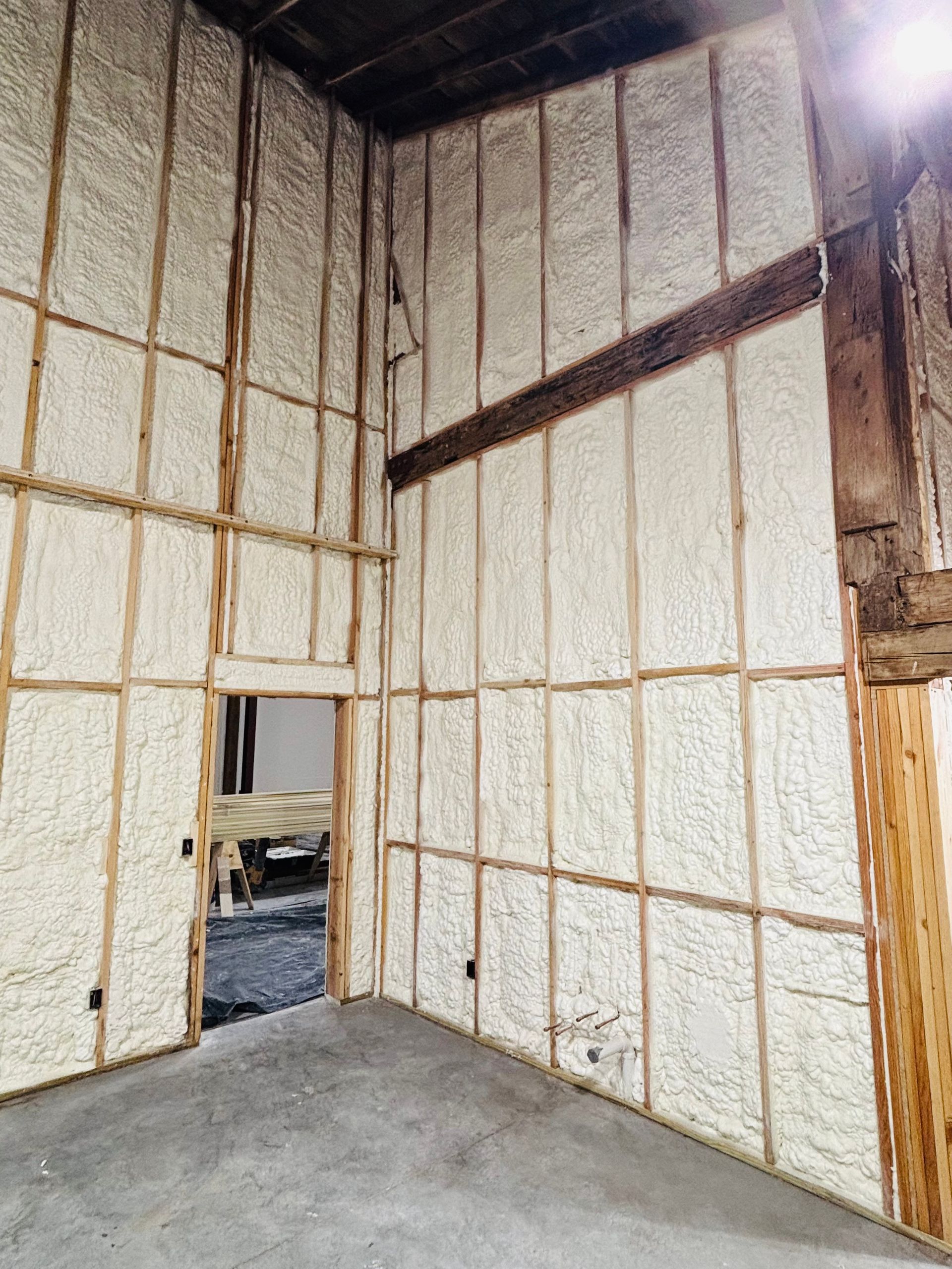 Interior view of a building's wooden frame walls filled with spray foam insulation, including a doorway.