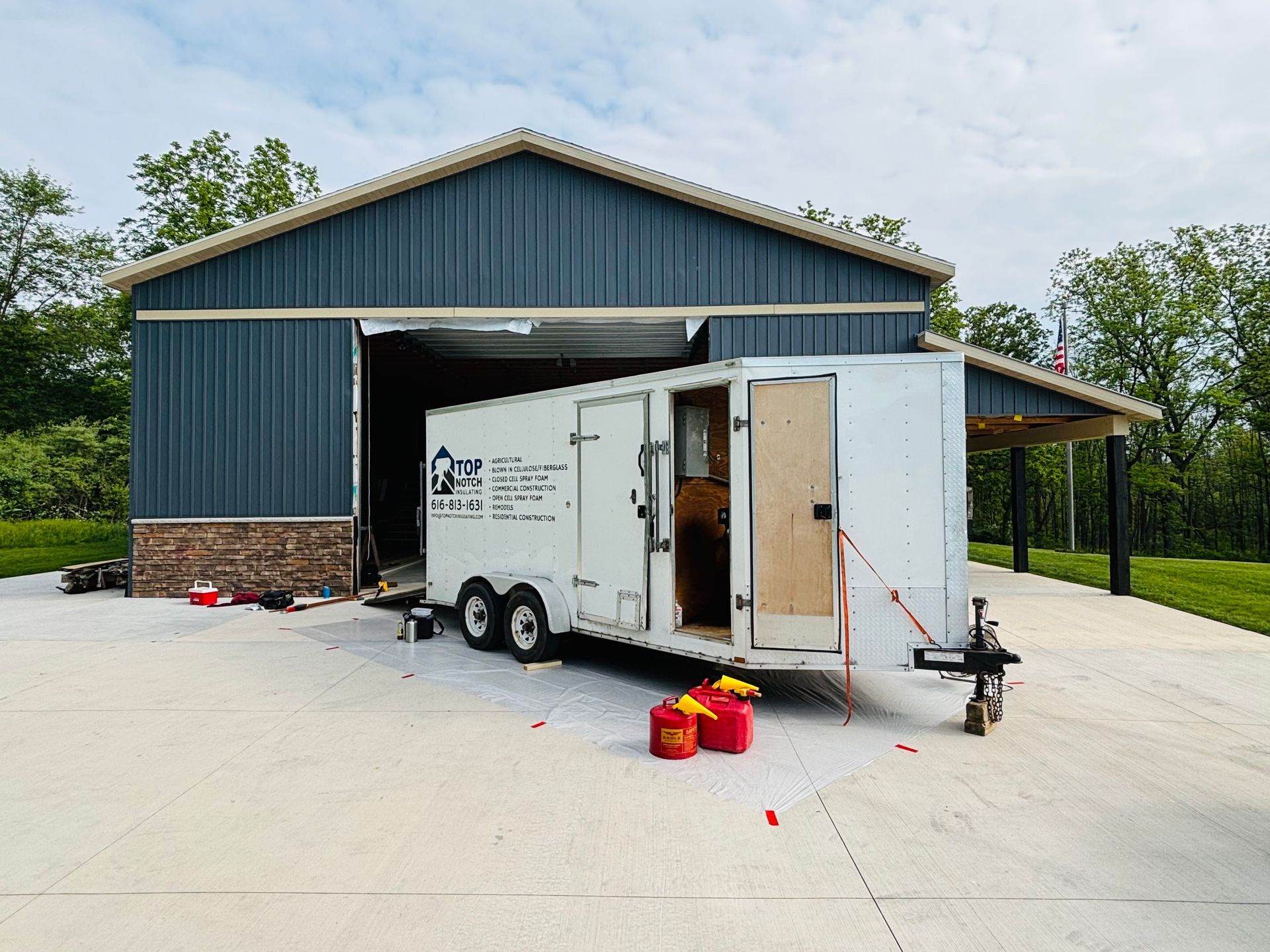 White trailer inside blue building, door open. Red containers on concrete.