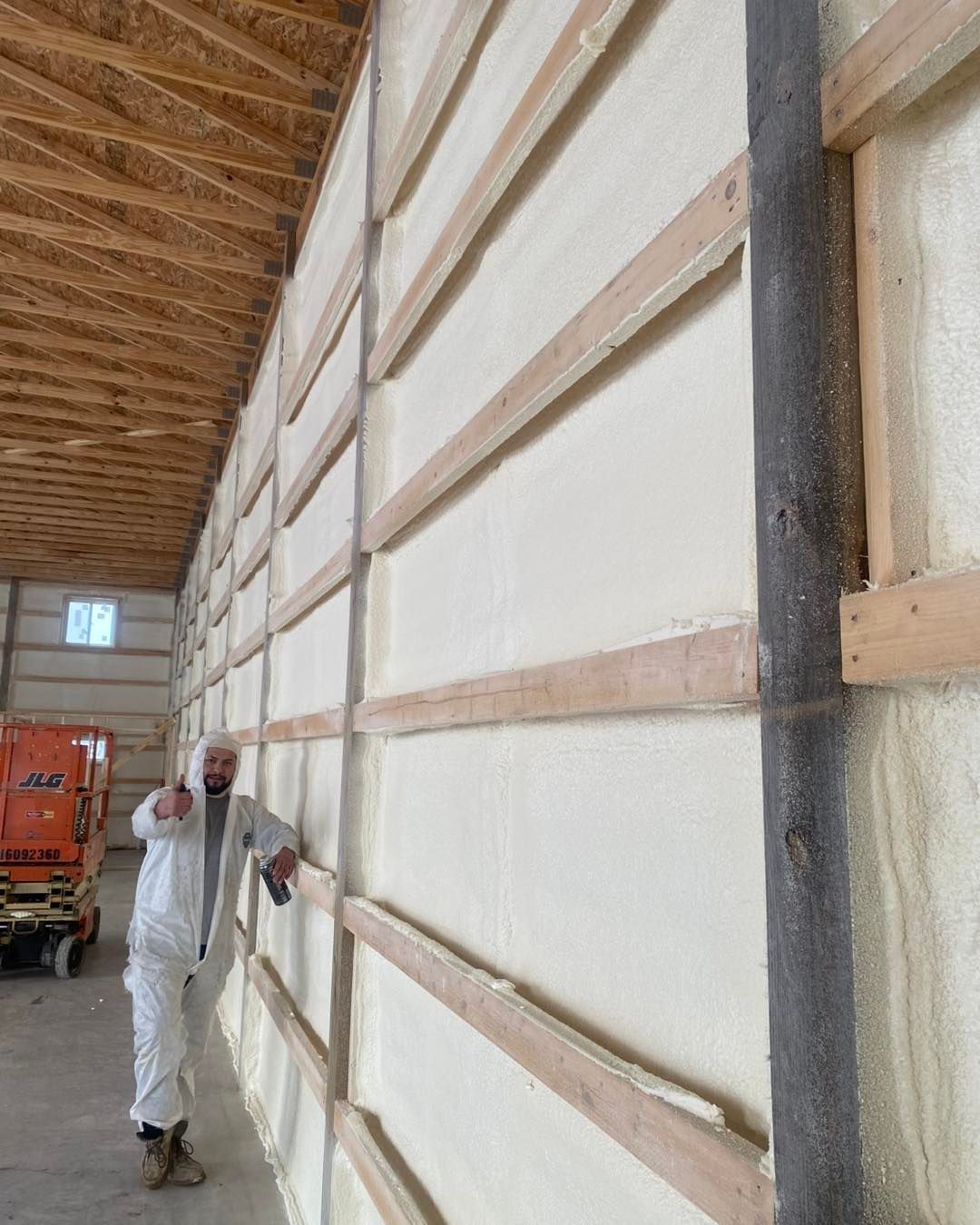 Man in protective suit inspecting spray foam insulation on a warehouse wall.